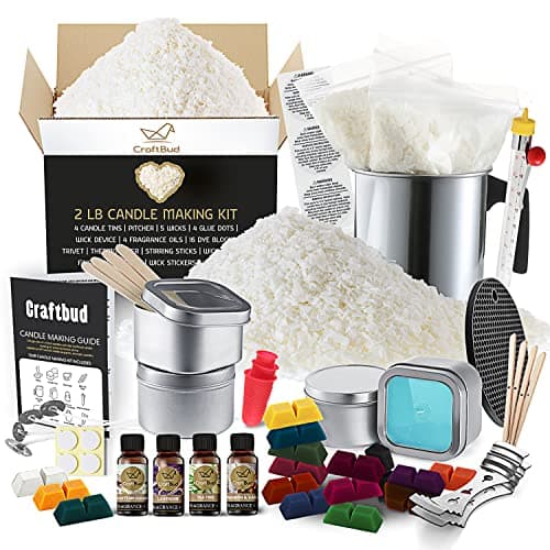 CraftBud candle making kit with soy wax flakes, colored dye blocks, fragrance oil bottles, wicks, metal tins, and melting pitcher laid out on a white surface